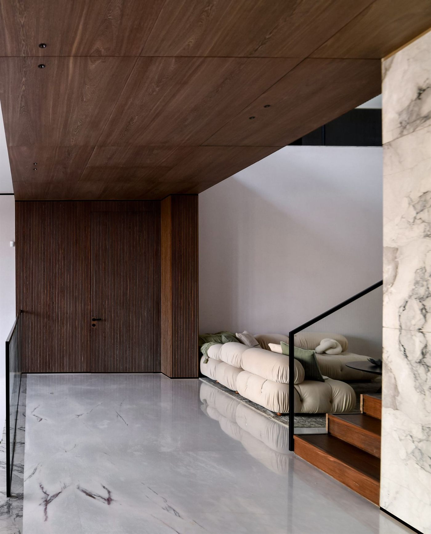 Recibidor con techo y muros de roble, piso de mármol y sofá modular color crema