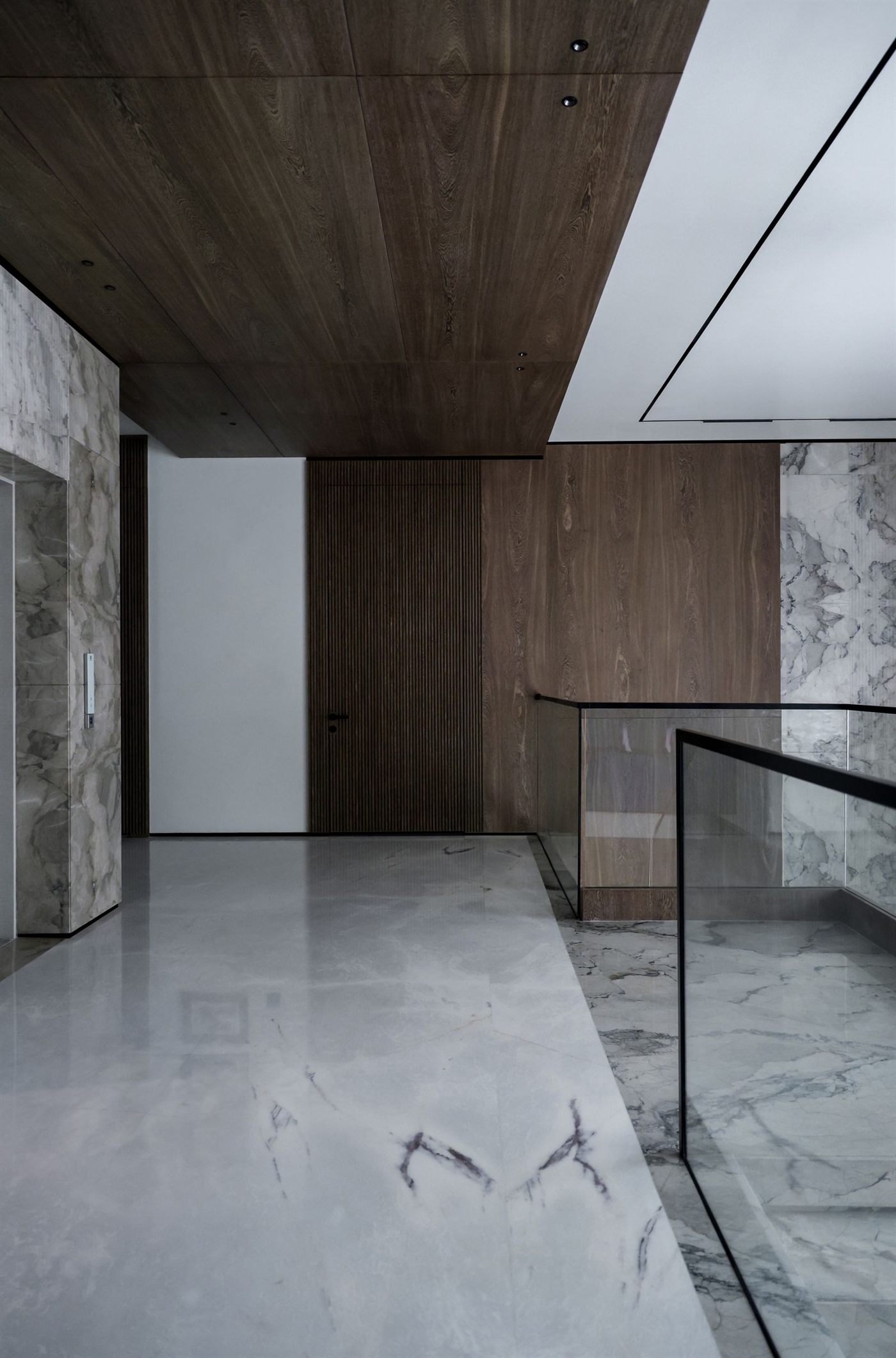 Pasillo interior con revestimiento de madera, muros de mármol y baranda de vidrio
