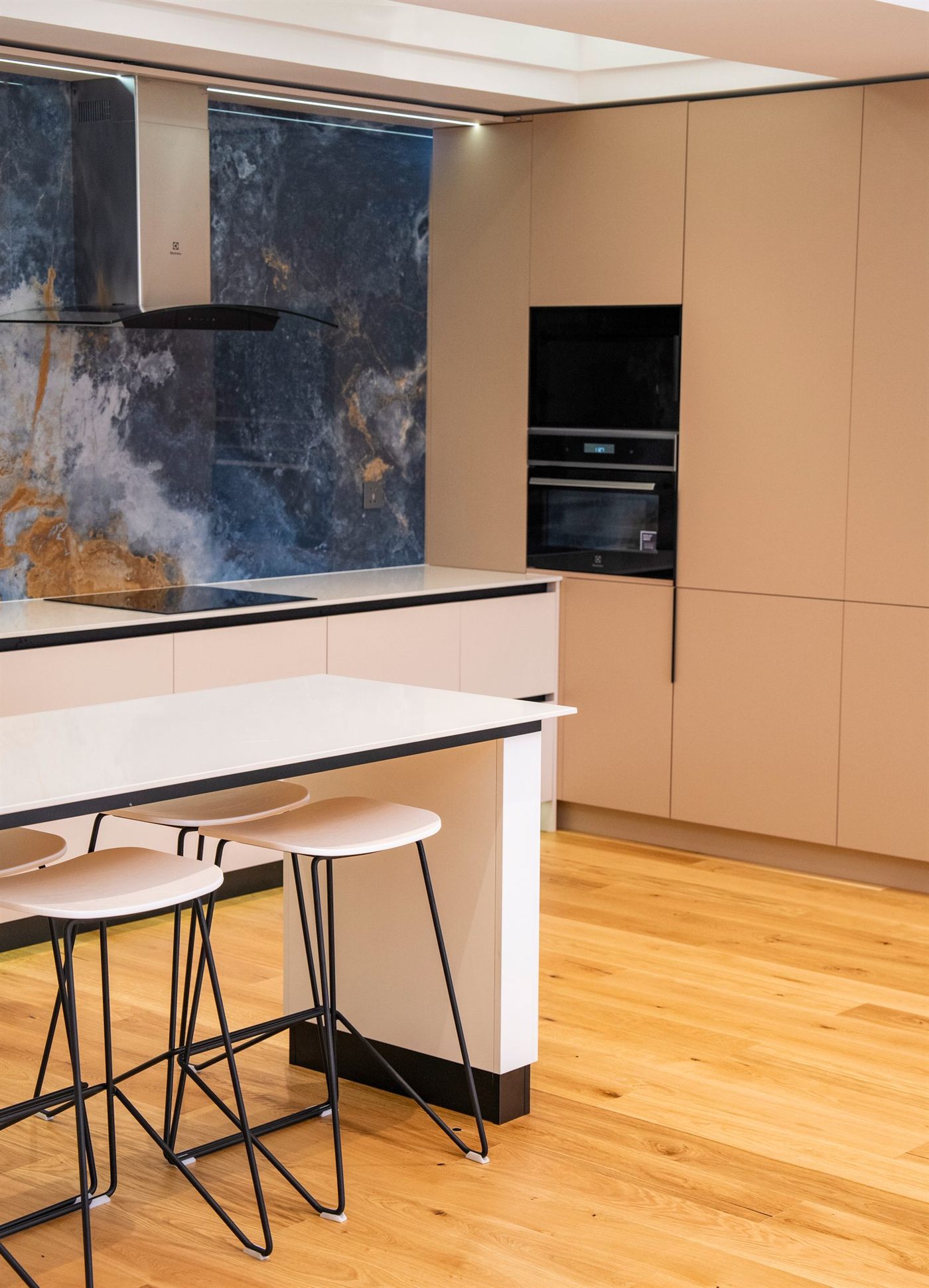 Cocina moderna con muebles color arena sin tiradores e isla blanca, frontal de piedra natural